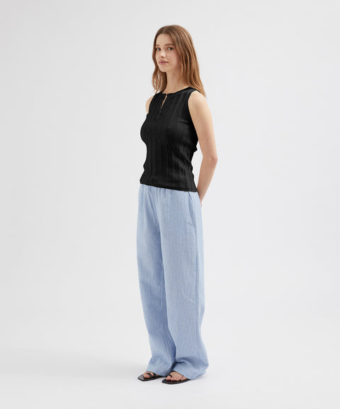 Woman wearing a black sleeveless top and light blue pants on a white background
