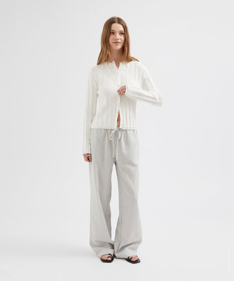 Woman wearing a white long-sleeve top and light gray pants on a white background