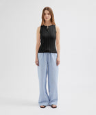 Woman wearing a black sleeveless top and light blue striped pants on a white background