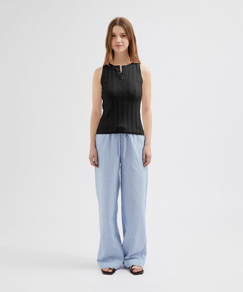 Woman wearing a black sleeveless top and light blue striped pants on a white background
