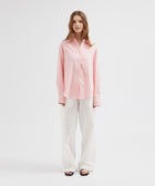Woman wearing a pink shirt and white pants on a white background