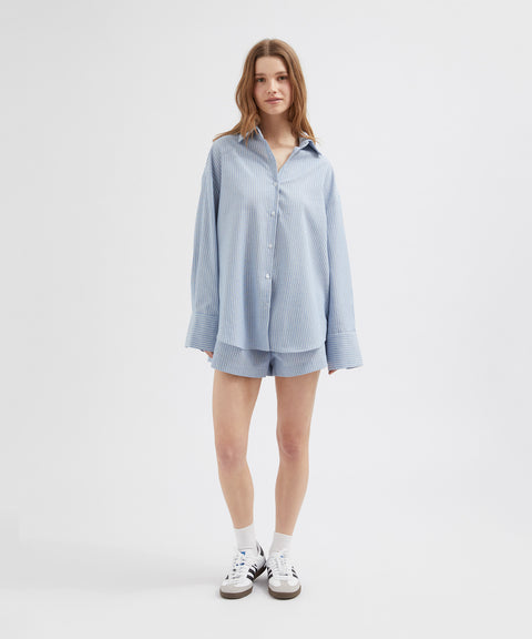 Woman wearing a light blue checkered shirt and shorts on a white background