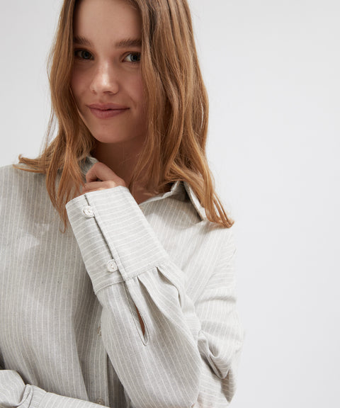 Woman wearing a light gray pinstripe shirt against a white background