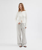 Woman wearing a white blouse and light gray pants on a white background