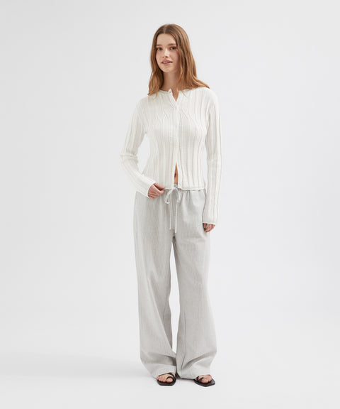 Woman wearing a white blouse and light gray pants on a white background