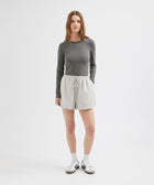 Person wearing a gray long-sleeve top and beige shorts on a white background