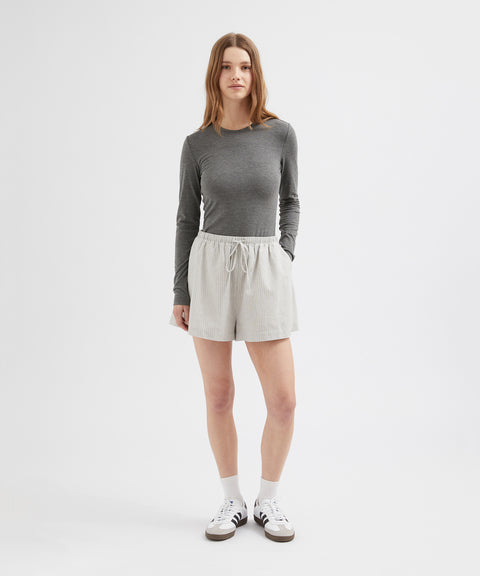 Person wearing a gray long-sleeve top and beige shorts on a white background