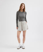 Woman wearing a gray long-sleeve top and light gray skirt on a white background