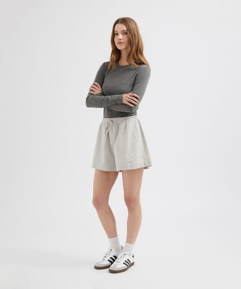 Woman wearing a gray long-sleeve top and light gray skirt on a white background