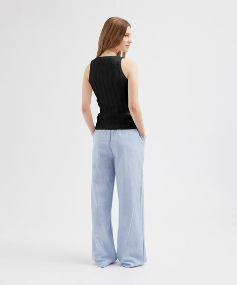 Woman wearing a black sleeveless top and light blue striped pants on a white background